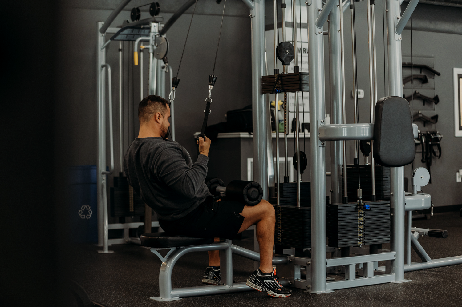 Josh DeMelo is seen sitting on a weight lifting machine, pulling down on straps to lift said weights, bracing his legs with a padded bar