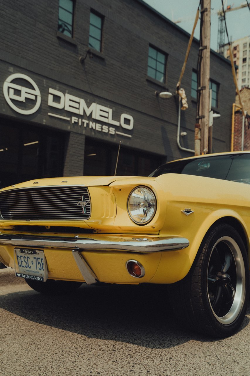 An older, yellow Mustang car parked outside of the DeMelo Fitness gym in London, Ontario