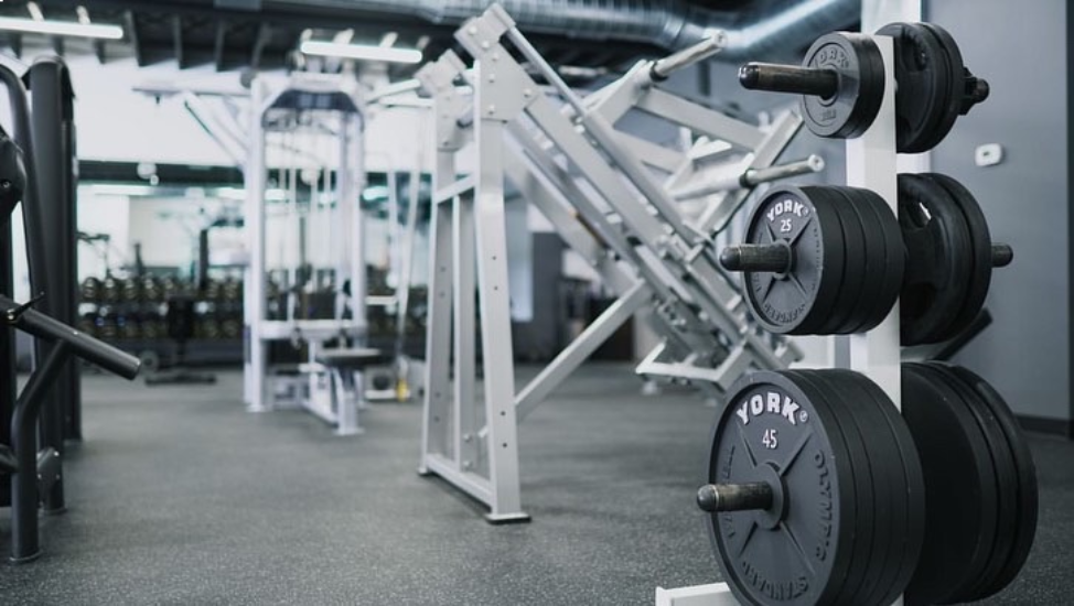 A rack of weights in the foreground with a slightly blurred background of gym equipment, with a wall of mirrors and hand weights in the very back